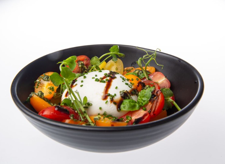 black bowl with cherry tomatoes, burrata and pea shoots, drizzled in balsamic glaze