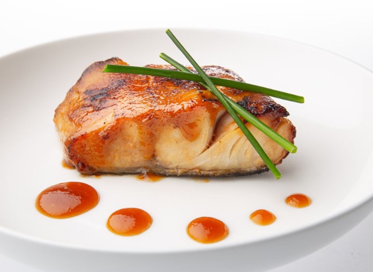 Glazed fish on a white plate garnished with chives